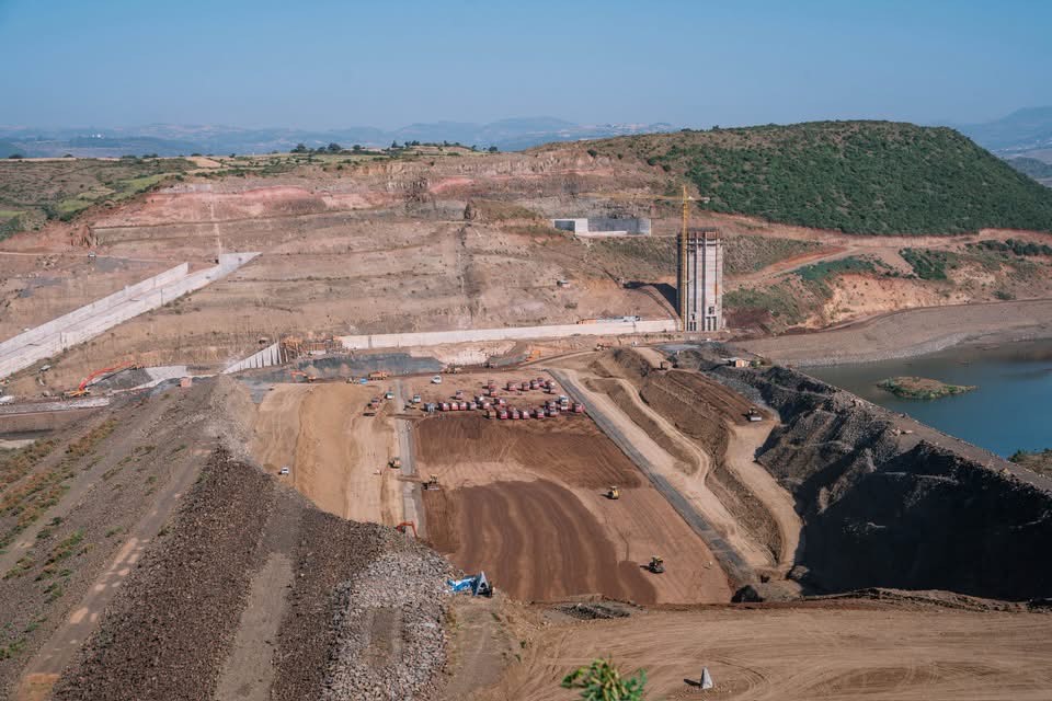 Abiy Ahmed Reviews New Amhara Dam Project: A Vital Step for Food Security Landscape photograph of Magatch Dam construction site in Gondar, Amhara region, with trucks and the river on the far right under a clear blue sky, marking a milestone in Ethiopia’s agricultural transformation and food security.